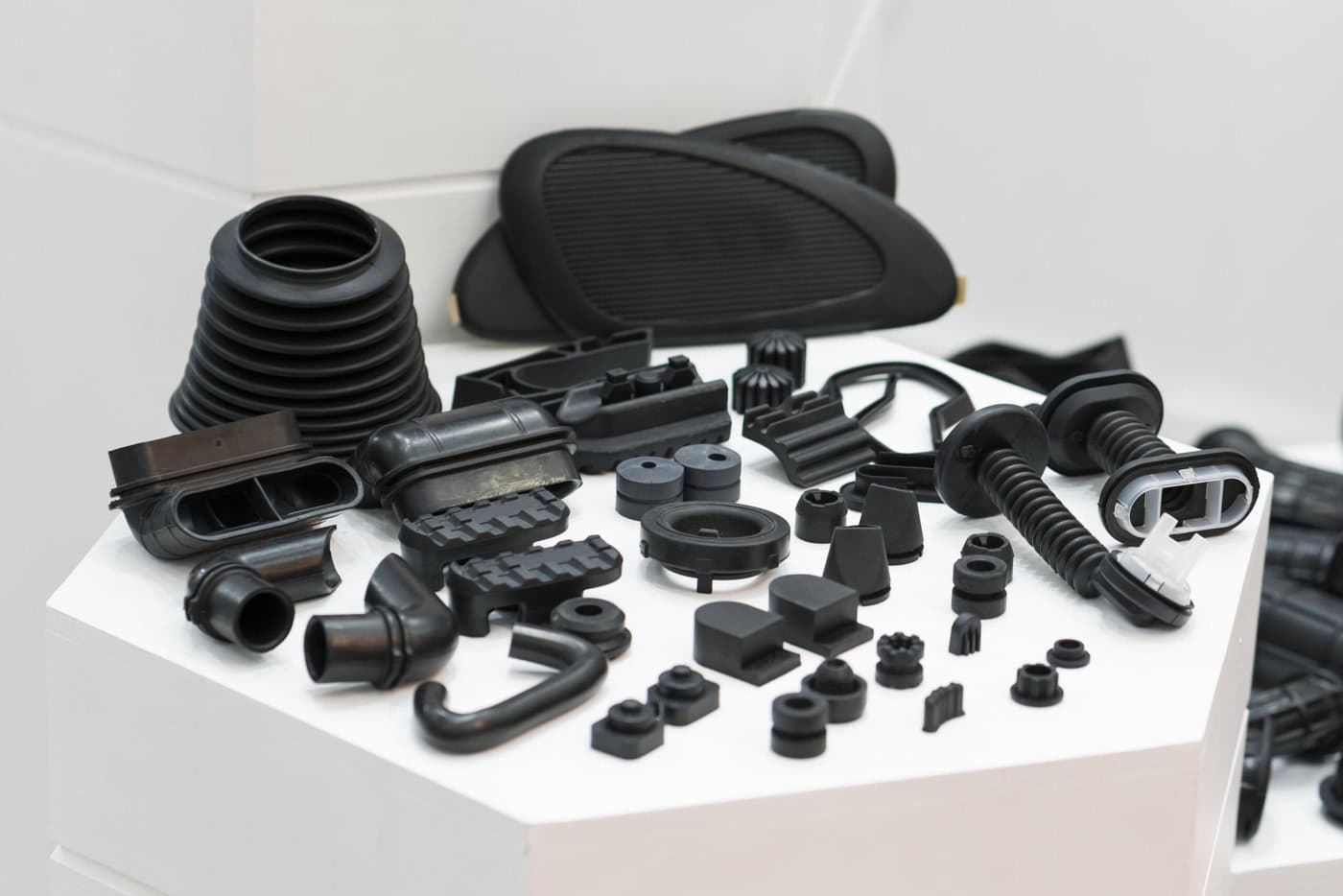 A display of various black rubber automotive parts, including hoses, grommets, and seals, arranged on a white surface. The parts are of different shapes and sizes.