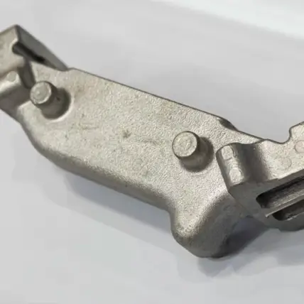A Close-Up Of A Metallic Mechanical Component With A Rough Texture, Featuring Two Cylindrical Protrusions And A Rectangular Cutout On The Right Side. The Component, Crafted Through Rapid Die Casting, Is Displayed On A White Surface.