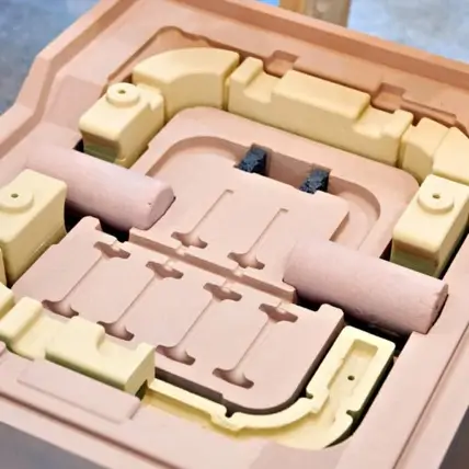 A Close-Up View Of A Sand Mold Used In Prototype Tooling And Metal Casting Processes. The Mold Features Various Intricate And Precisely Shaped Cavities And Pathways, Designed To Form Detailed Parts Once The Molten Metal Is Poured In And Solidified.