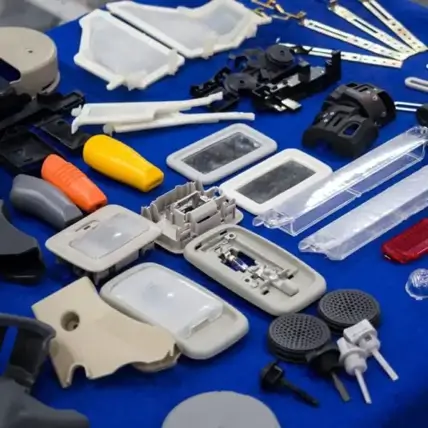 A Variety Of Plastic And Metal Parts Displayed On A Blue Surface. The Items Include Handles, Casings, Brackets, Gears, And Electronic Components. Some Parts Are Rectangular While Others Are Irregularly Shaped, Appearing To Be Components Of Different Tools Or Devices Created Using Our Urethane Casting Service.