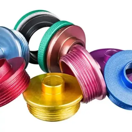 A Collection Of Brightly Colored, Metal Threaded Plugs Arranged In A Scattered Manner. The Plugs Are In Various Colors Including Blue, Green, Red, Pink, Purple, Gold, And Copper, Each Featuring Distinct Textures And Designs.