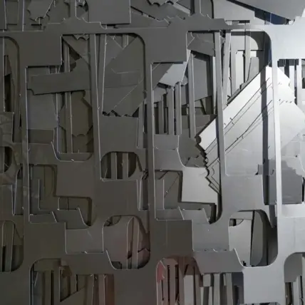 A Close-Up Image Of Various Abstract Metal Cutouts, Likely Produced Using Prototype Laser Cutting, Arranged In A Layered Manner. The Cutouts Feature Different Shapes And Sizes, Creating A Complex, Textured Pattern. The Overall Color Of The Metal Is A Muted Gray, With Subtle Light Reflections Highlighting The Contours.