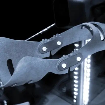 A Close-Up Image Of Sleek, Modern Prosthetic Fingers With Articulated Joints And A Strappy Design, Crafted Using Mjf 3D Printing Service. The Background Is A Dark Setting Illuminated With Reflective Lights, Highlighting The Metallic Components And Craftsmanship Of The Prosthetic Parts.