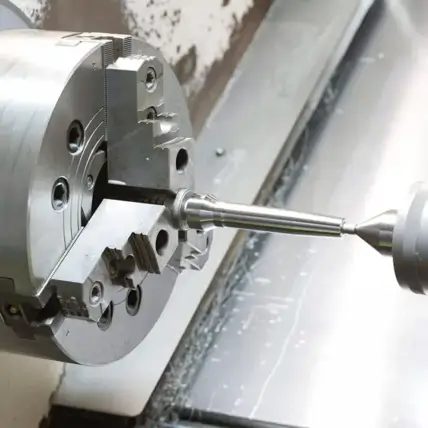 A Close-Up View Of A Cnc Lathe Machine Working On A Metal Prototype. The Component Is Held Firmly In The Chuck While A Cutting Tool Shapes It Precisely. The Setup Is In A Clean Industrial Environment With Metallic Surfaces Visible In The Background.