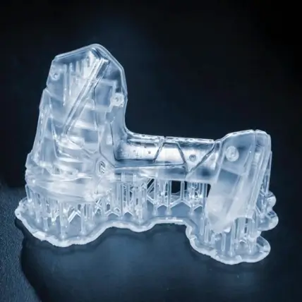 A Transparent 3D Printed Model Of A Mechanical Part With Intricate Details, Created Using A Polyjet 3D Printing Service, Is Supported By A Lattice Structure At Its Base And Displayed Against A Dark Background.