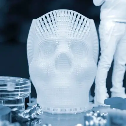 A Close-Up Of A 3D-Printed Skull Displayed On A Surface, Created Using A Polyjet 3D Printing Service, Surrounded By Various Indistinct Objects. To The Right, A Partially Visible Human Figure Stands, Also Seemingly 3D-Printed. The Scene Is Rendered In A Monochromatic Blue Tone.
