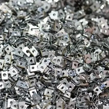 A Close-Up Of A Large Pile Of Shiny, Small, Metallic Square Nuts With Threaded Holes In The Center, Created Through Precise Die Cutting. The Nuts Are Arranged In A Scattered, Overlapping Manner, Creating A Textured And Reflective Surface.
