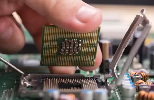 Close-Up Of A Hand Installing A Central Processing Unit (Cpu) Into A Socket On A Motherboard. The Focus Is On The Cpu With Its Pins Visible, And Other Components Of The Motherboard Can Be Seen In The Background.