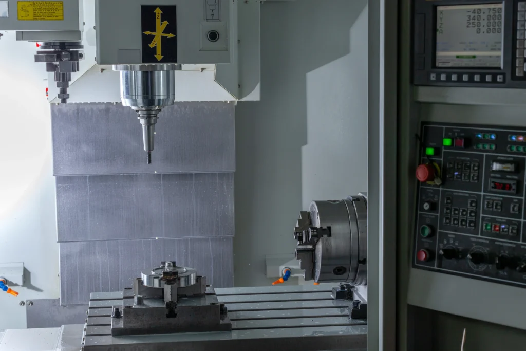 A Modern Cnc Machine With A Spindle In The Center, Control Panel To The Right, And A Workpiece Secured On The Bed. The Interior Is Well-Lit, Showcasing Mechanized Components Used For Precise Manufacturing Tasks.