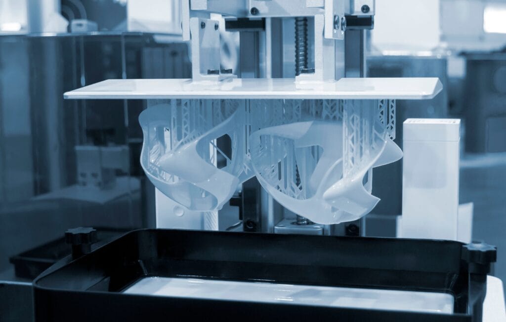 A Close-Up View Of A 3D Printer Creating A Complex, Curved Structure. The Scene Has A Blue Tint, Highlighting The Intricate Design And Technology. The Printer Is Shown In The Midst Of The Printing Process.