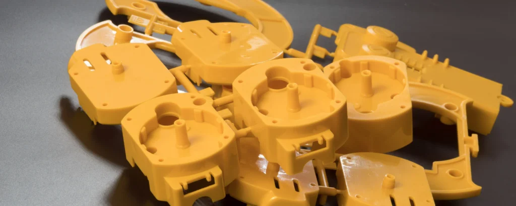 Close-Up Of Scattered Yellow Plastic Components With Various Shapes And Slots, Placed On A Dark Surface. The Pieces Appear To Be Parts Of A Larger Assembly Or Mechanical Structure.