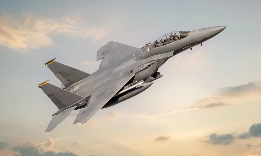 A Gray Fighter Jet Soars Through A Partly Cloudy Sky During Sunset, Showcasing Its Aerodynamic Design And Powerful Engines. The Sky Features Soft Orange And Blue Hues, Enhancing The Dramatic Appearance Of The Scene.