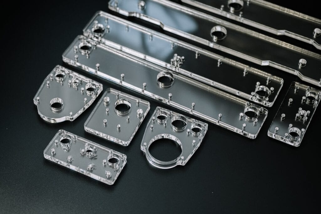 A Collection Of Transparent Acrylic Or Plastic Components With Precise Holes And Cutouts Arranged On A Dark Surface. The Pieces Vary In Size And Shape, Suggesting Parts For An Assembly Or Prototype.