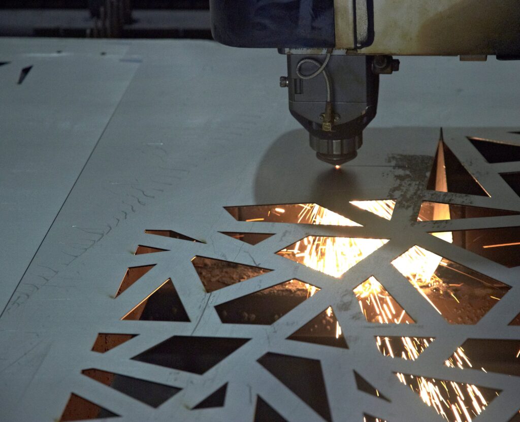 A Close-Up Of A Laser Cutting Machine Slicing Through A Sheet Of Metal, Creating An Intricate Geometric Pattern. Bright Sparks Fly From The Precise Cut, Highlighting The Precision And Technology Involved In The Process.