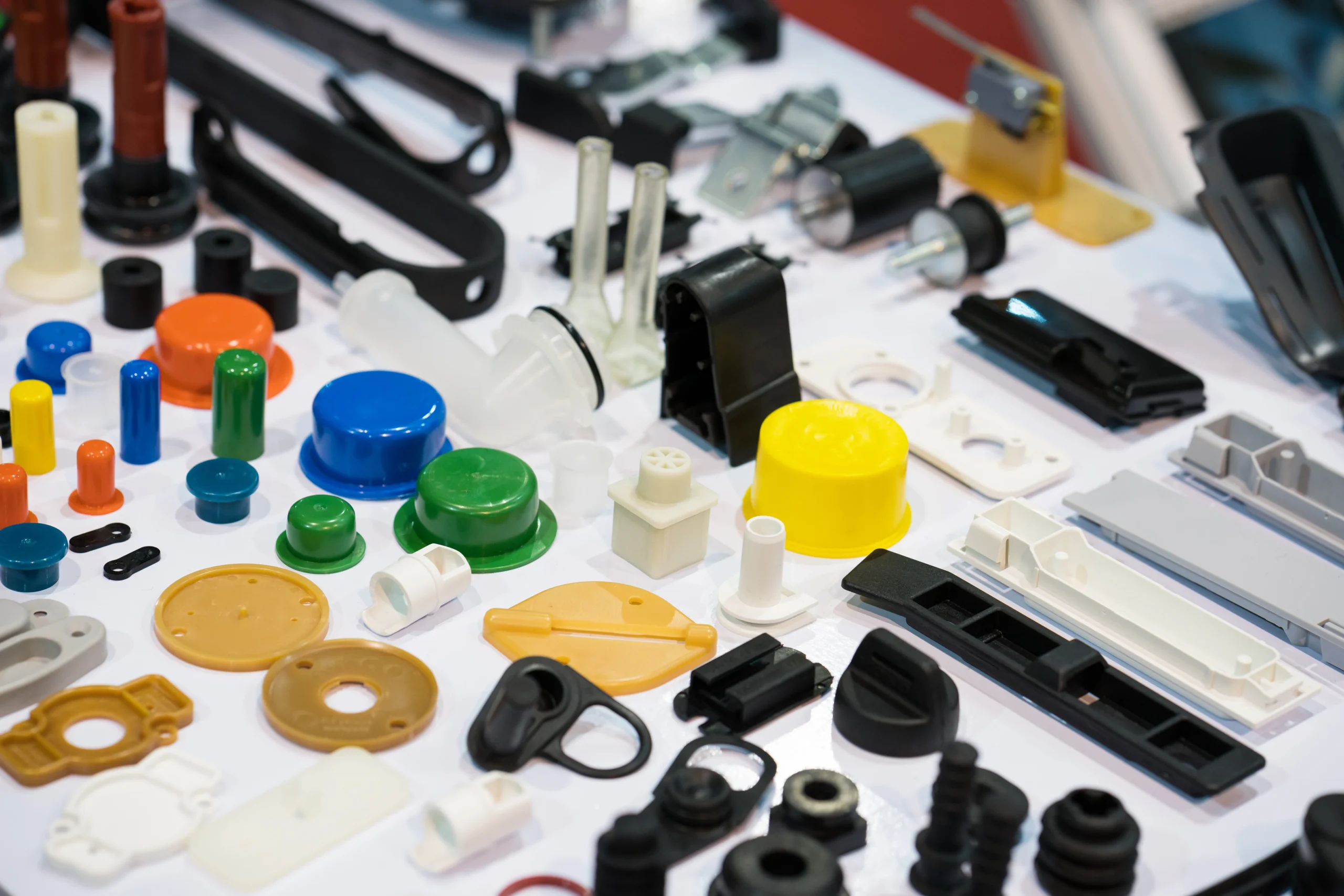 Assorted plastic and metal components displayed on a flat surface, including various shapes and colors, such as round, rectangular, and cylindrical pieces in red, blue, yellow, green, and black.