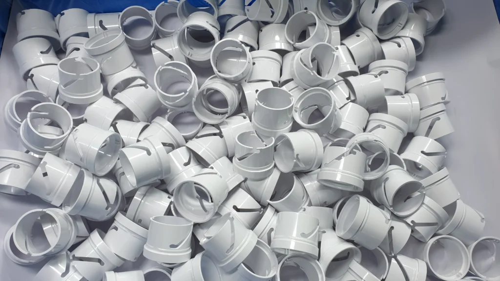 A Pile Of White Plastic Caps, Each With A Circular Shape And A Protruding Latch Mechanism, Haphazardly Stacked In A Box. The Caps Are Uniformly Designed And Appear To Be Components For A Larger Item Or Machine.