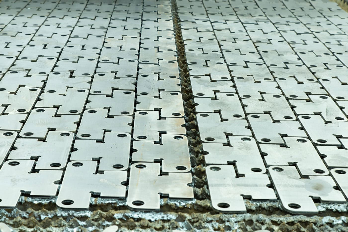 A Close-Up View Of Interlocking Metal Plates With A Grid-Like Pattern, Reminiscent Of Aerospace Prototyping Services. The Plates Form A Continuous Surface With Visible Joints And Grooves, Displaying A Weathered Texture.