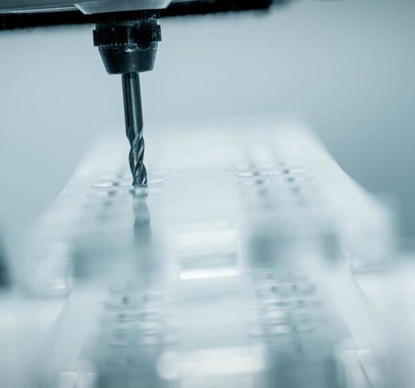 Close-Up Of A Cnc Machine Drill Bit Shaping A Clear Block, Showcasing The Precision And Focus Of Acrylic Cnc Machining Service Against A Blurred Background.