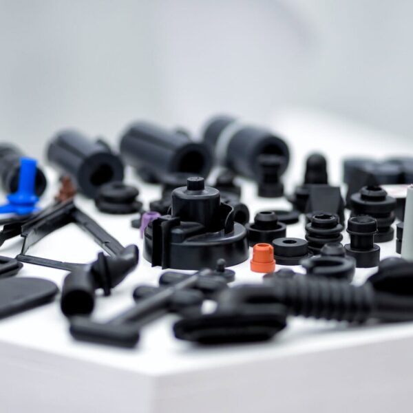 A Variety Of Small, Black Plastic Components And Connectors Created With Abs Cnc Machining Service Are Scattered On A White Surface, With A Few Pieces In Orange And Blue. The Background Is Blurred, Focusing On The Parts.