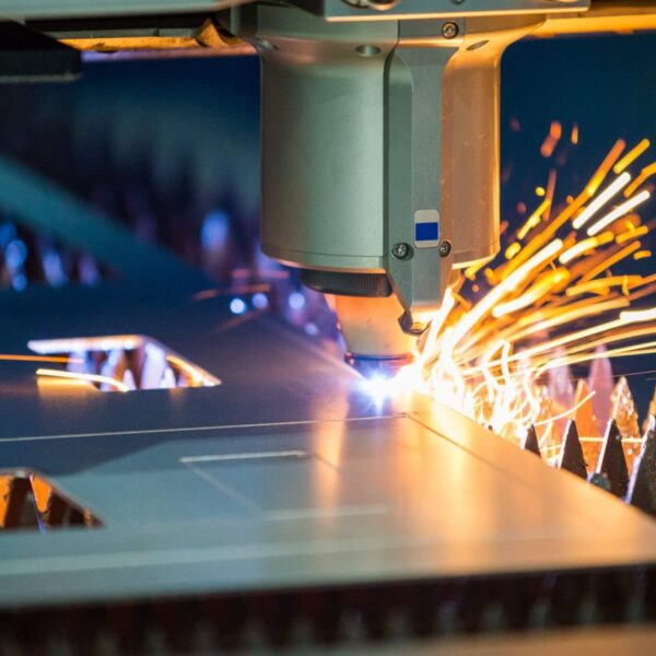 A Close-Up Of A Laser Cutting Machine Slicing Through A Stainless Steel Sheet, With Bright Sparks Flying From The Contact Point, Surrounded By Sharp Metal Edges And Geometric Cutouts Typical Of Sheet Metal Fabrication.