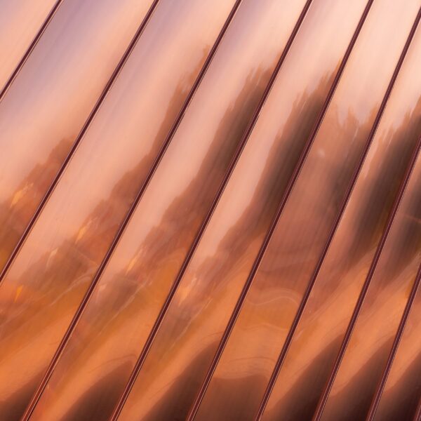 Close-Up Of A Shiny, Copper-Colored Metal Surface With Diagonal Ridges And Soft Reflections, Creating An Abstract, Wavy Pattern.