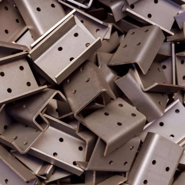 A Pile Of Custom Metal Brackets, Each Rectangular With Several Holes, Stacked Haphazardly. These Brackets Appear To Be Components For Construction Or Assembly Purposes.