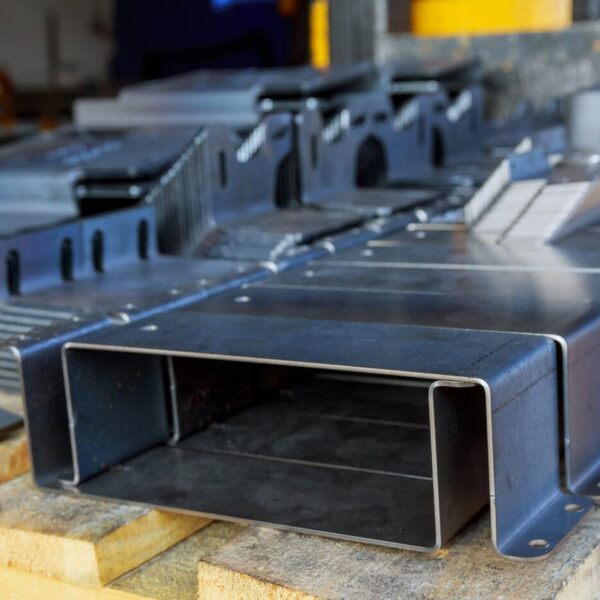 Close-Up View Of Several Custom Sheet Metal Enclosures With Holes And Bends Stacked On A Wooden Pallet, Likely Prepared For Industrial Use Or Assembly In A Workshop Or Factory Setting.