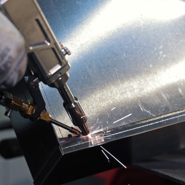 A Close-Up Of A Worker Using A Welding Tool To Join Two Metal Sheets For Custom Sheet Metal Enclosures, With Sparks Flying From The Contact Point. The Worker'S Gloved Hand Is Visible Holding The Tool.